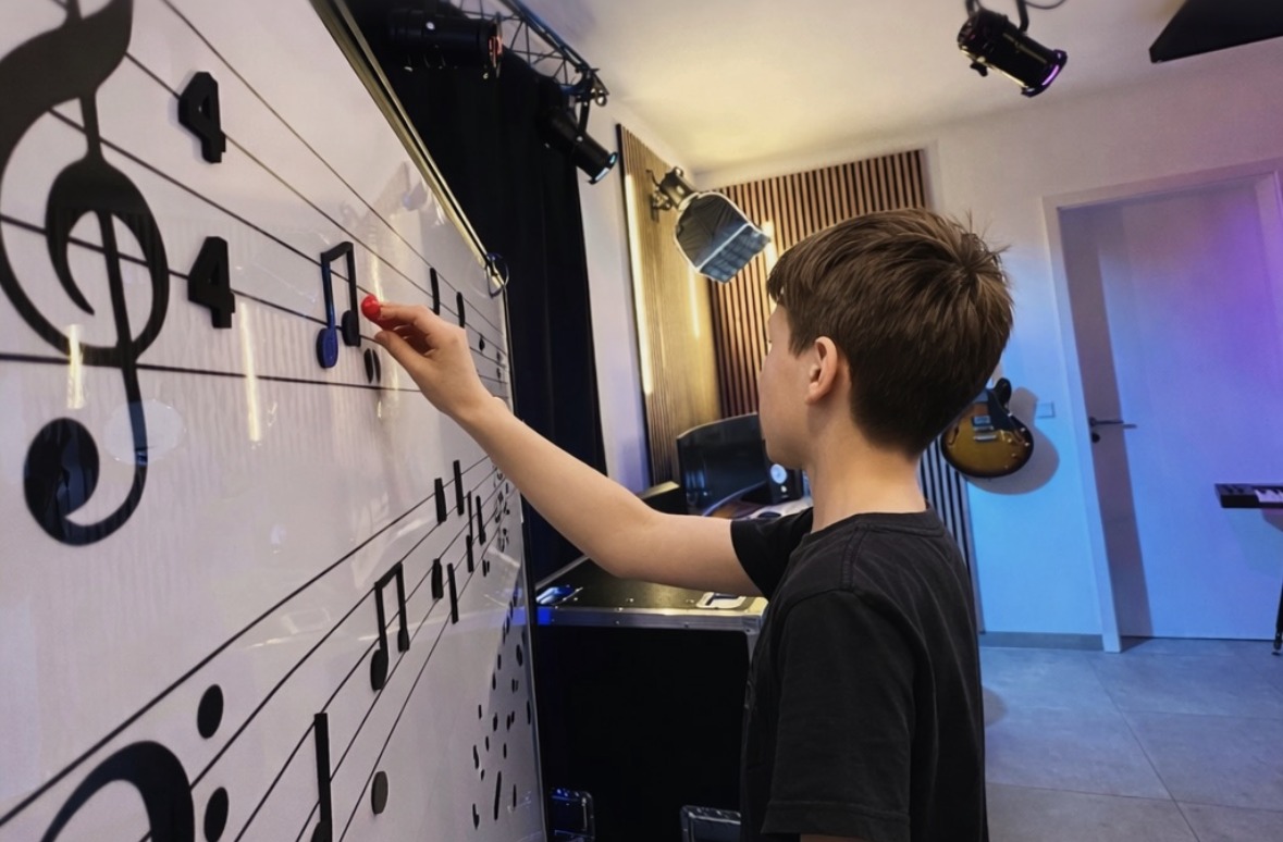 Ein Junge legt von der Seite gesehen eine magnetische Note auf die große Notentafel mit Violin- und Bassschlüssel